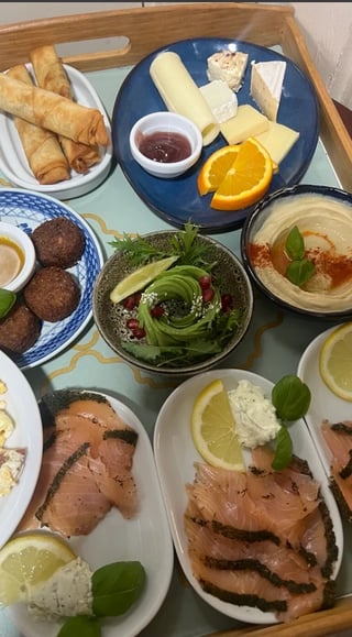 Overhead view of a Mediterranean charcuterie board with cured meats, cheese, bread, salad, hummus, and fresh citrus on a wooden tray