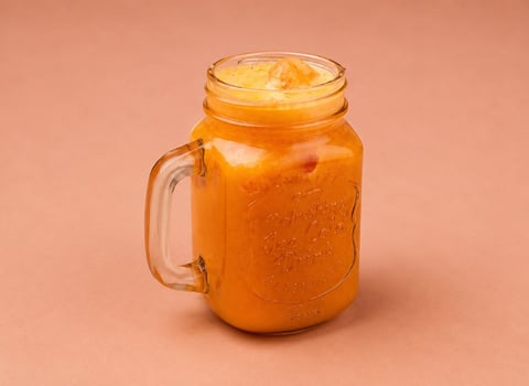Mason jar filled with orange beverage and ice cubes on a peach-colored background