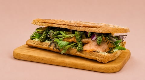Gourmet sandwich with grilled chicken, fresh greens, and purple onions on a crusty baguette, served on a wooden board