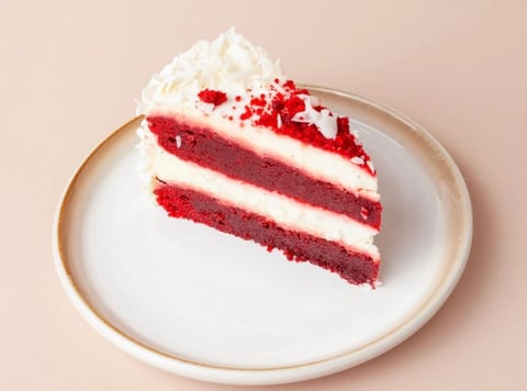 Slice of red velvet cake with white frosting and cream cheese topping on a white plate