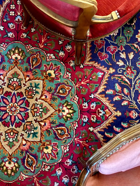 Ornate colorful rugs with intricate floral patterns in jewel tones displayed together with decorative chair visible above