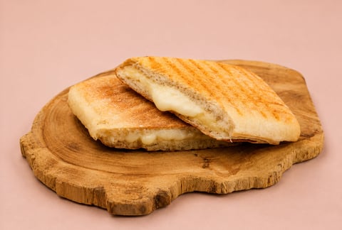 Two grilled paninis with melted cheese filling on a wooden serving board against a pink background