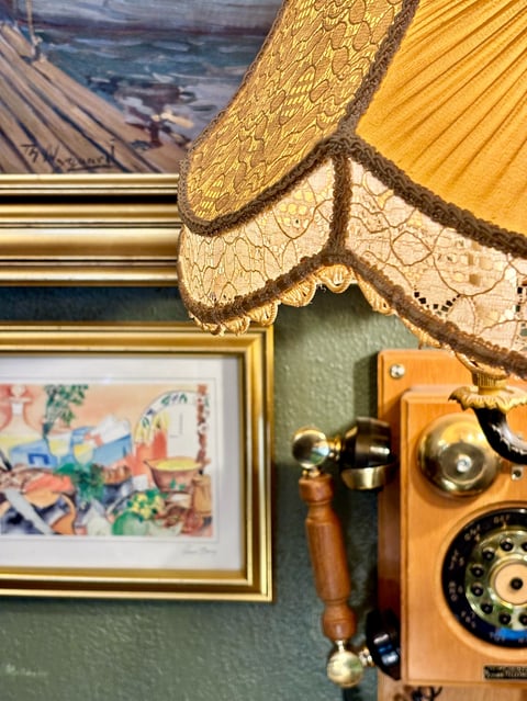Vintage rotary telephone and framed artwork on green wall with ornate gold lampshade above