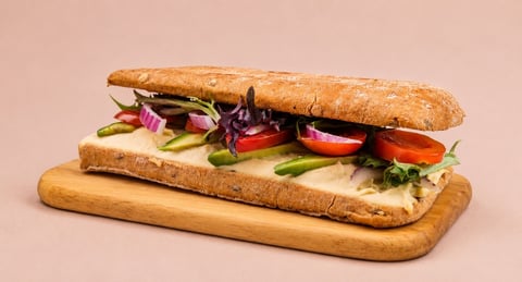 Gourmet sandwich on artisan bread with fresh vegetables, purple cabbage, tomato, and greens on a wooden board against beige background
